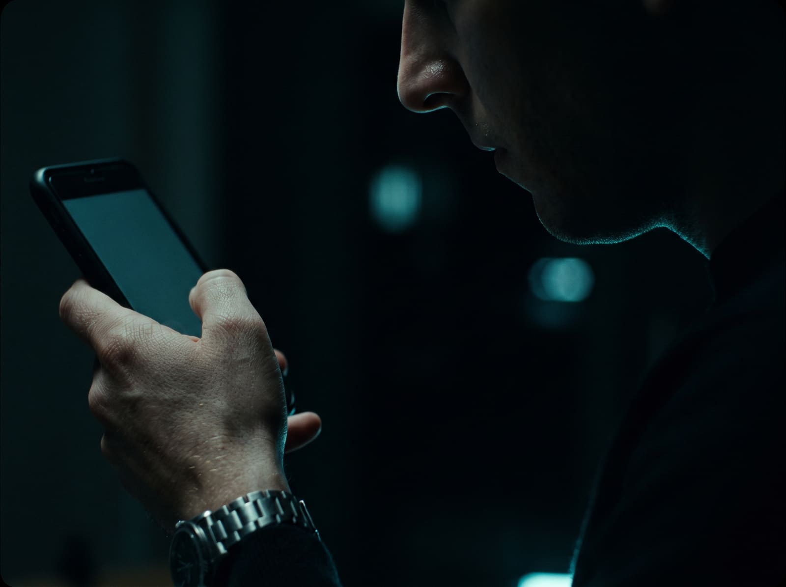 A phone screen throwing cyan light onto a hand in a dark room.